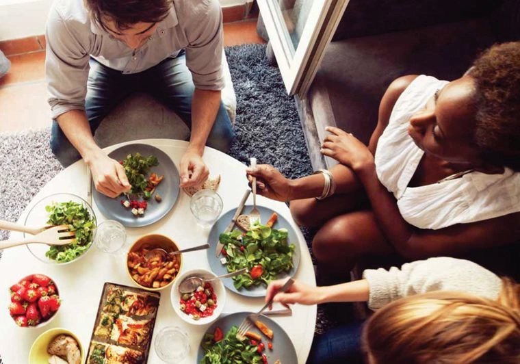 pessoas comendo salada envolta de uma mesa redonda 
