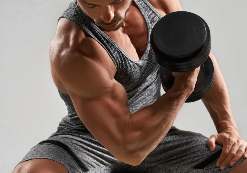 homem forte sentado fazendo musculação mostrando seus bíceps