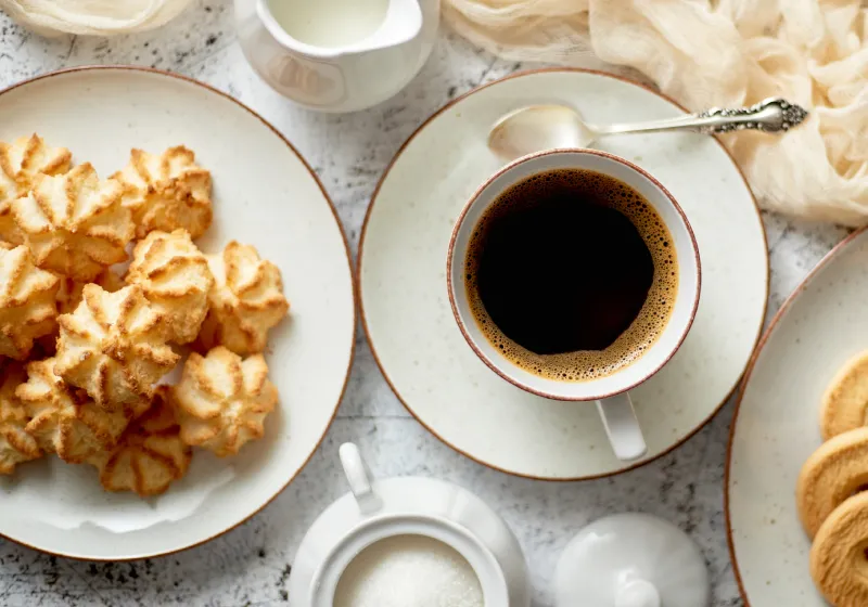 mesa com biscoitos de coco proteico com café preto e bolachas de coco no prato