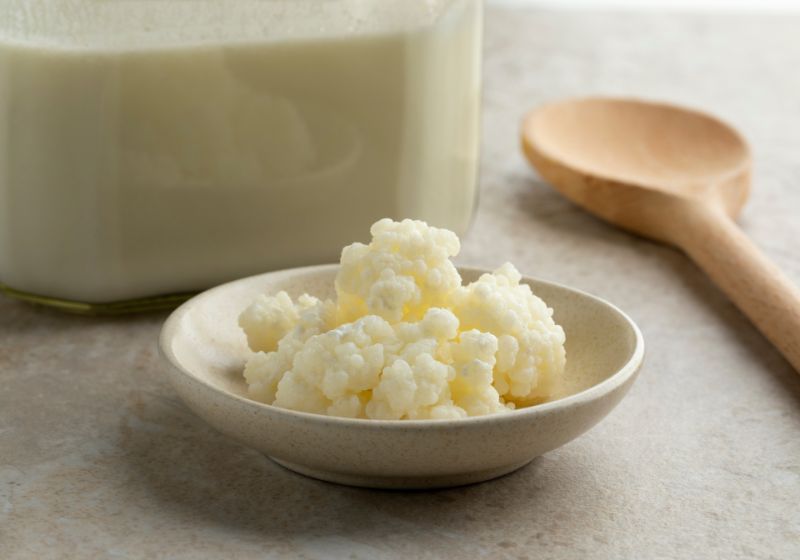 pote com Kefir dentro em cima de uma mesa e do lado uma colher de pau 