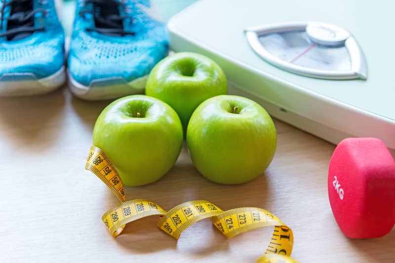 mesa com maçãs, fita métrica, peso de academia, balança e tênis de corrida