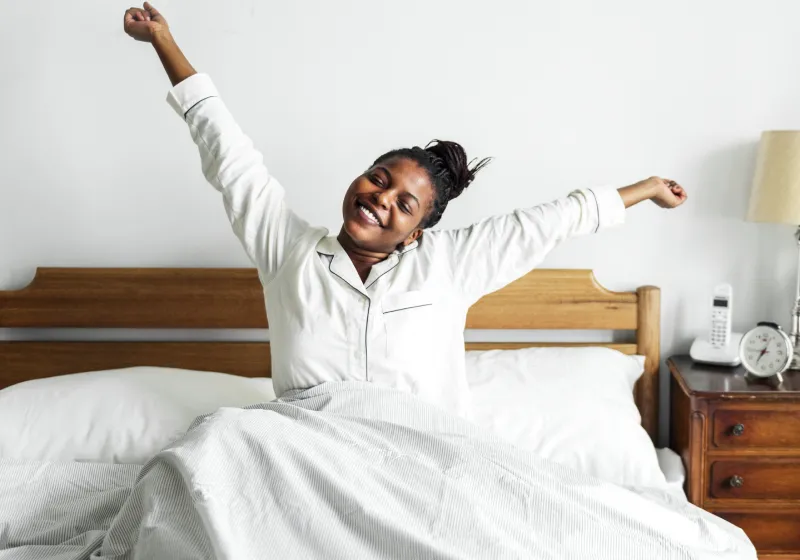mulher negra acordando se espreguiçando sentada na cama 
