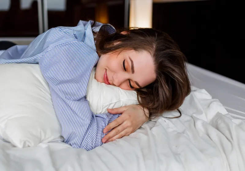 linda mulher sorridente deitada na cama abraçando travesseiro 