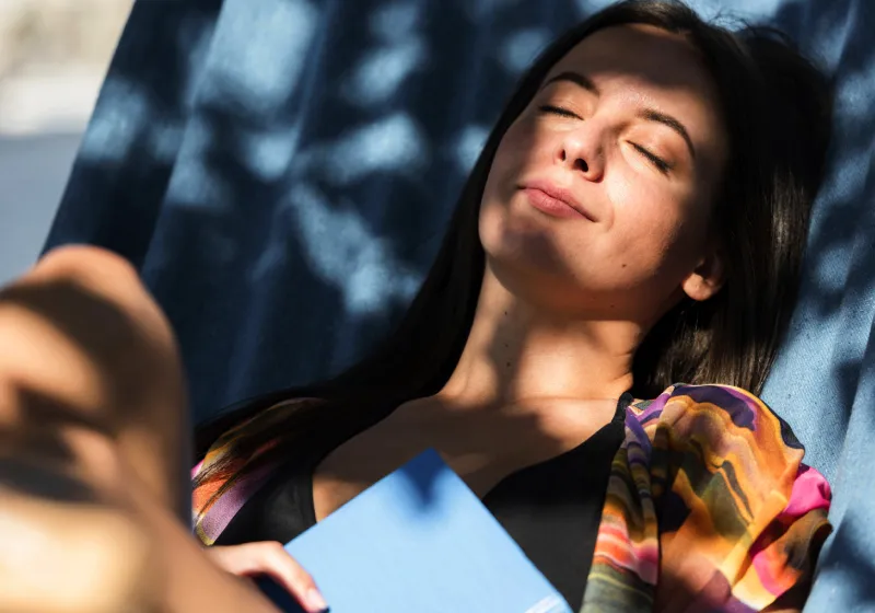 mulher relaxando na rede enquanto com um livro no sol 