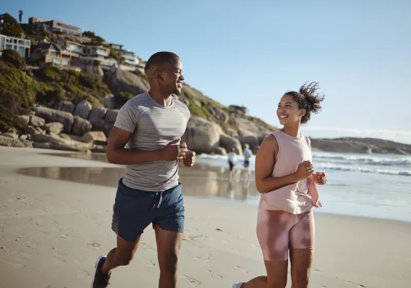 casal fitness sorridente correndo na praia 