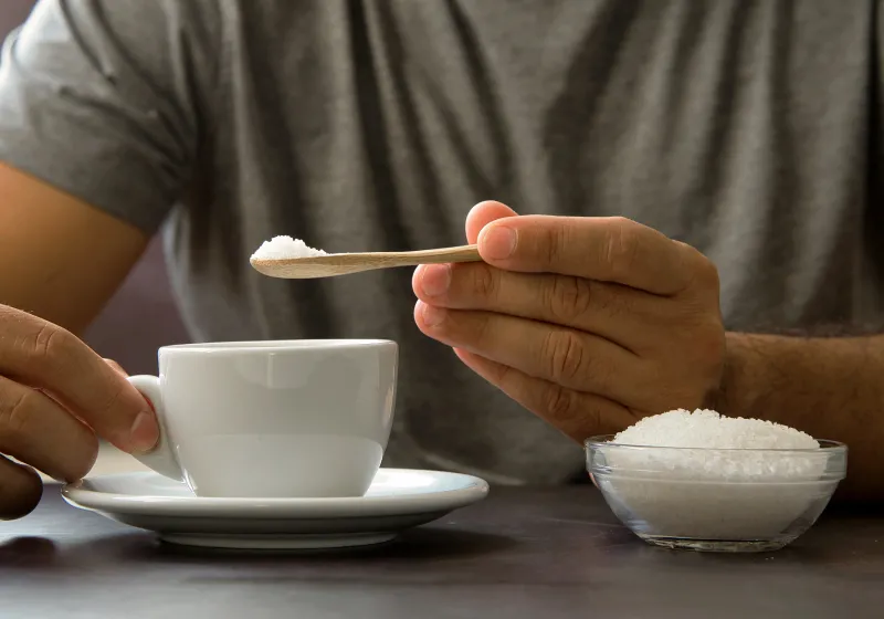 mão masculina segurando colherzinha de madeira com açúcar para colocar na xícara