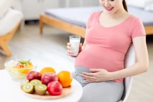 mulher grávida sentada na cadeira tomando leite e comendo frutas