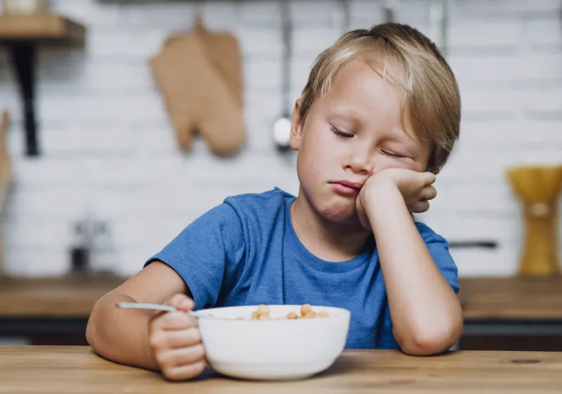 garoto desanimado não querendo comer seus cereais na mesa 