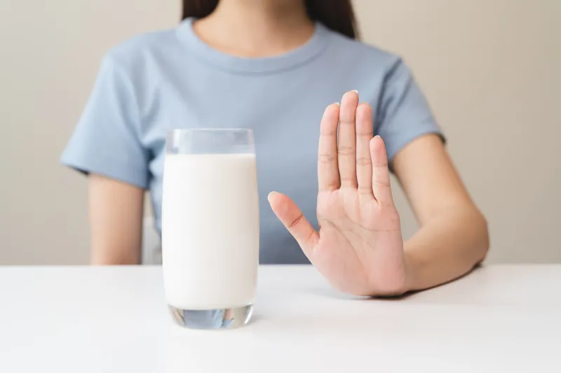 mulher sentanda na mesa negando um copo de vidro com leite 