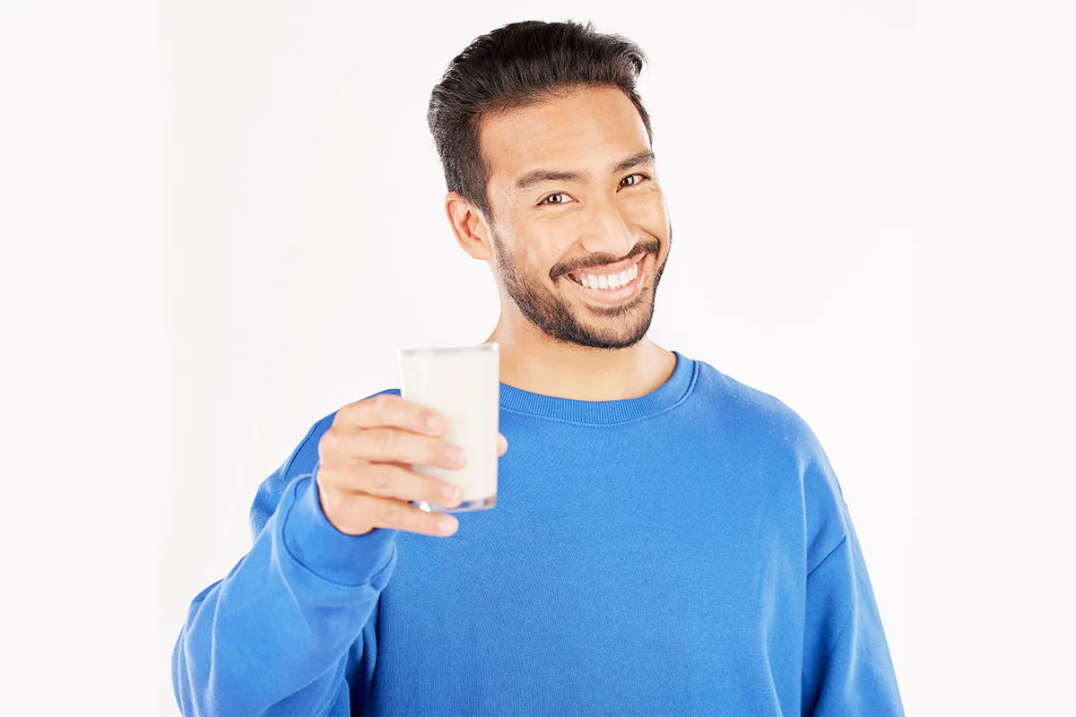 homem com moletom azul sorrindo com copo de leite na mão