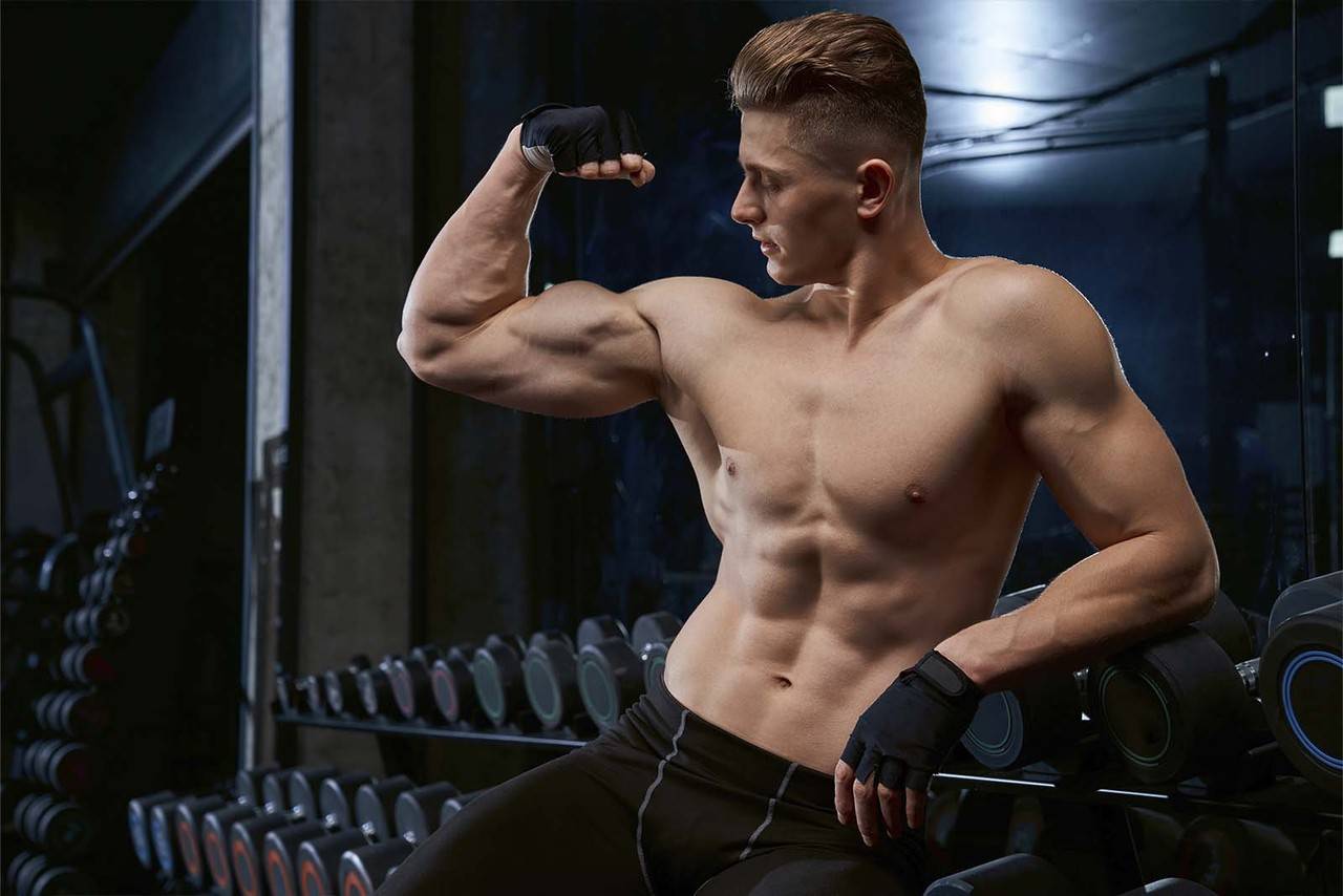 homem sem camisa na academia mostrando os efeitos do pump no bíceps do braço esquerdo