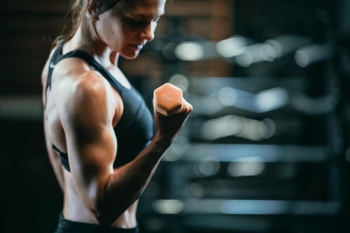 Mulher com roupa de academia fazendo treino de superiores com halter