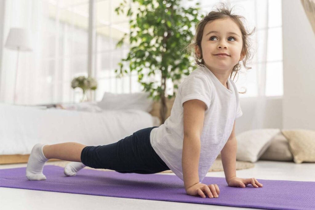 Imagem de uma menina fazendo o exercício de prancha, em cima de um tapete roxo no chão, vestindo roupas de praticar exercício, com o fundo de sala de estar de dia 