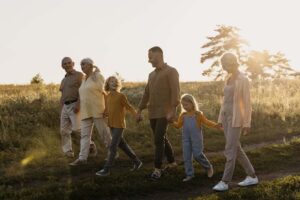 Imagem de uma família com avós, pais e crianças contentes andando juntas e de mãos dadas em um campo, durante o por do sol.