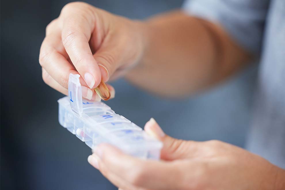 uma pessoa organizando os medicamentos em um recipiente transparente com os dias da semana separados  