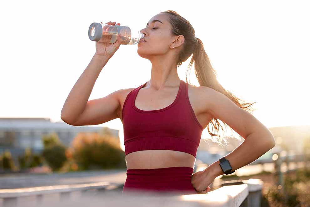 uma mulher se hidratando após fazer uma corrida em final de tarde