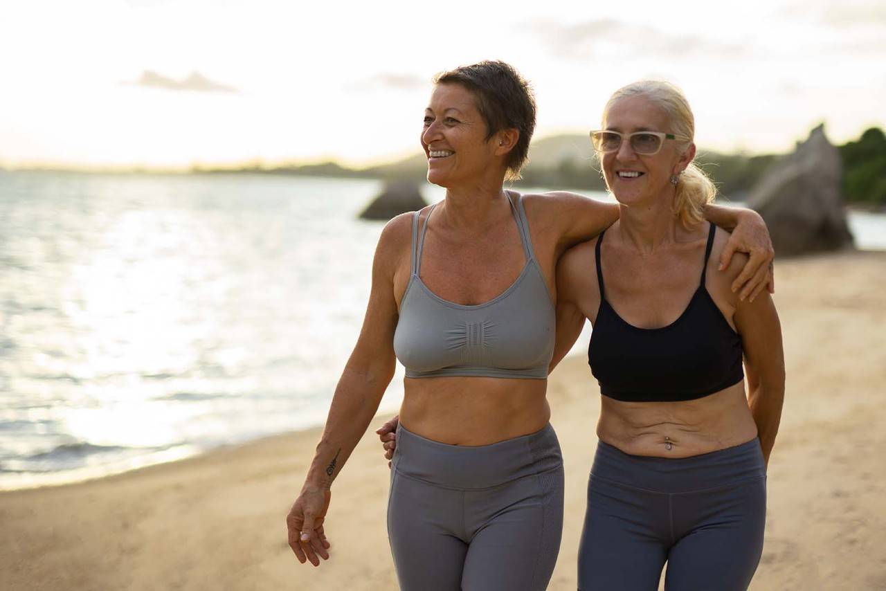 Imagem de uma dupla de senhoras fazendo uma caminhada na praia de manhã