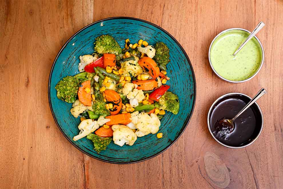 um prato com legumes e molhos ao lado dentro de um prato de ceramica e dois pequenos bowls em cima de uma mesa