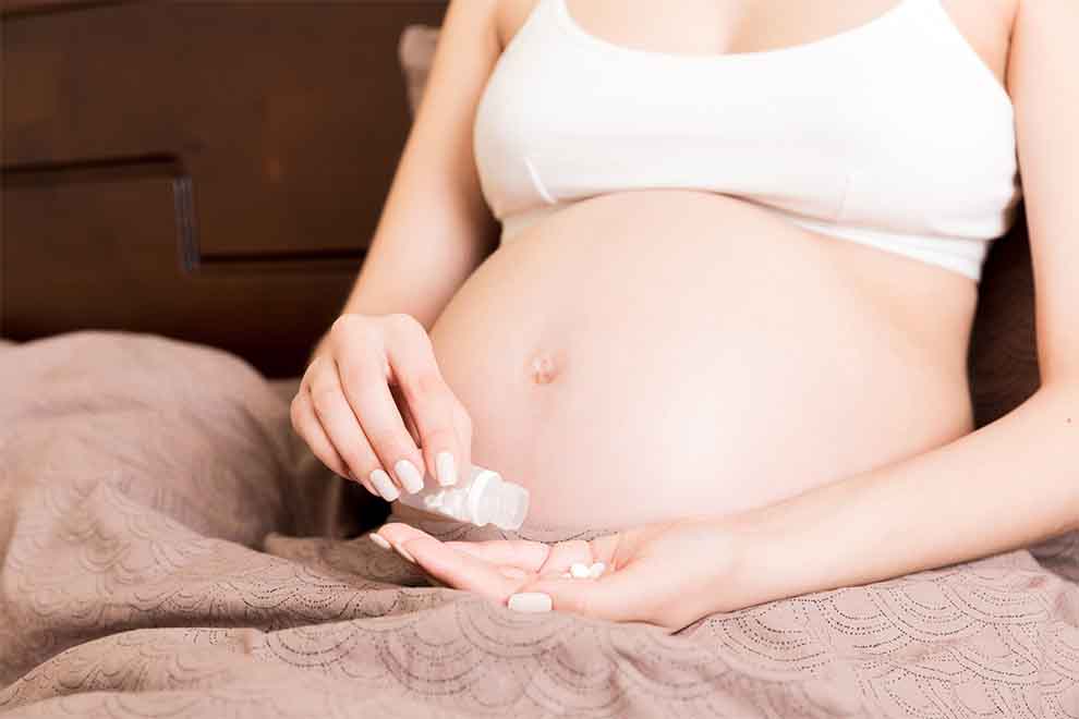 uma mulher grávida tomando suplementos sentada no sofá em um dia ensolarado