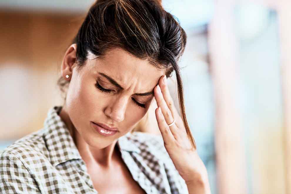 uma mulher com um mão na testa com enxaqueca em sua casa